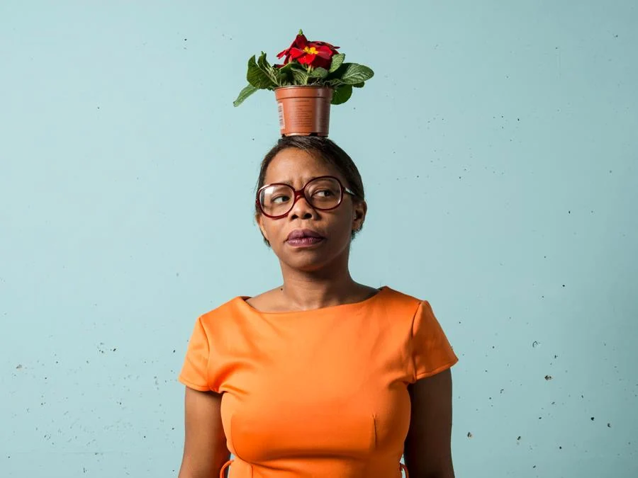 Elena Brocolitch en robe orange, une fleur en pot posée sur la tête
